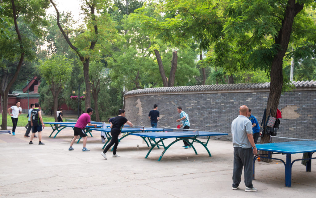 BEIJING, CHINA - MAY 19, 2016. Group of Chinese city dwellers Beijing are playing in the park in the table tennis against the background of the wall and the trees